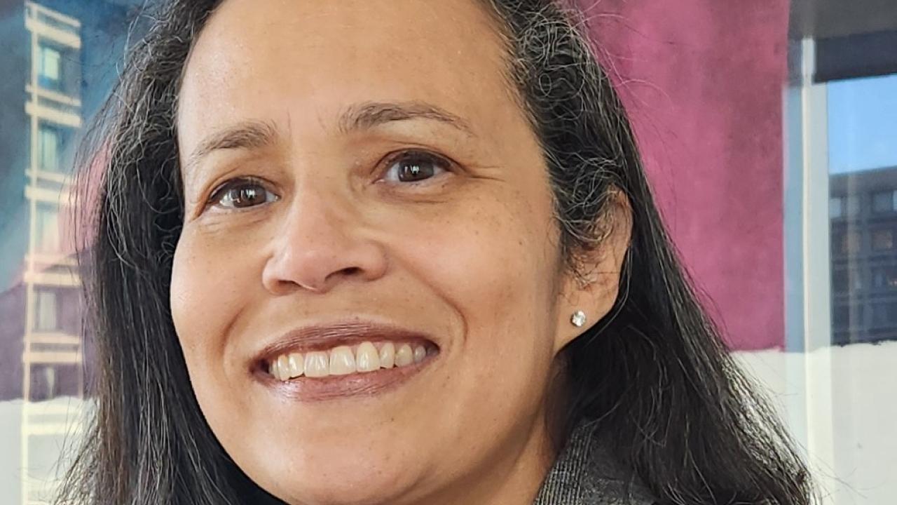 Headshot of Ann Morning in a gray suit jacket against an abstract blue and pink background.