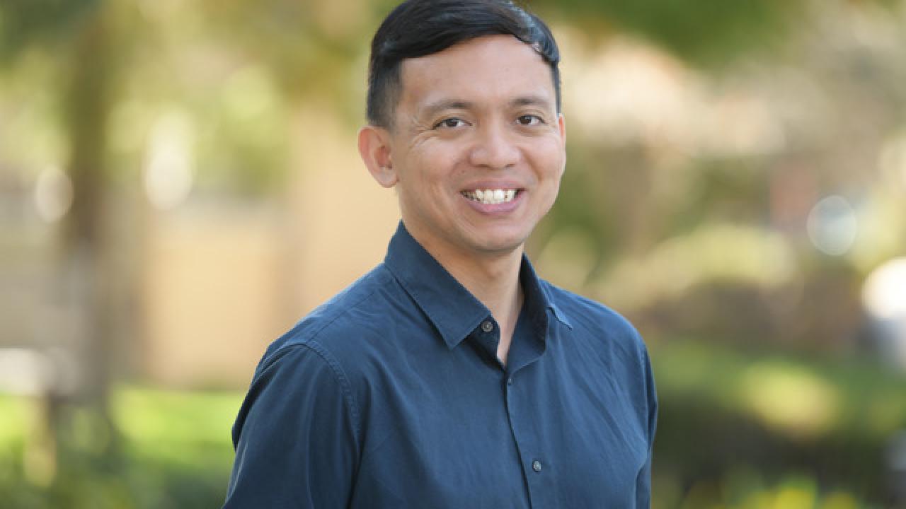 Headshot of Amir Aziz wearing a dark blue shirt with blurred trees and greenery in the background.