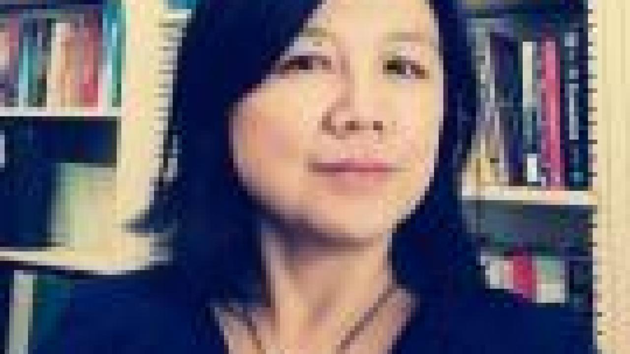 Headshot of Xiaoling Shu wearing a black top and turquoise necklace with books in the background.