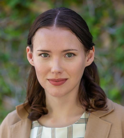 A headshot of a caucasian woman with shoulder length brown wavy hair.