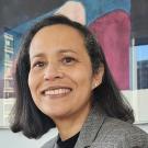 Headshot of Ann Morning in a gray suit jacket against an abstract blue and pink background.