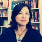 Headshot of Xiaoling Shu wearing a black top and turquoise necklace with books in the background.