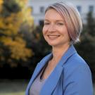 Headshot of Nadia Smiecinska wearing a blue blazer. Trees and a building are in the background. 