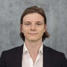 Headshot of Evan Baughman in white button down and black blazer against a gray background